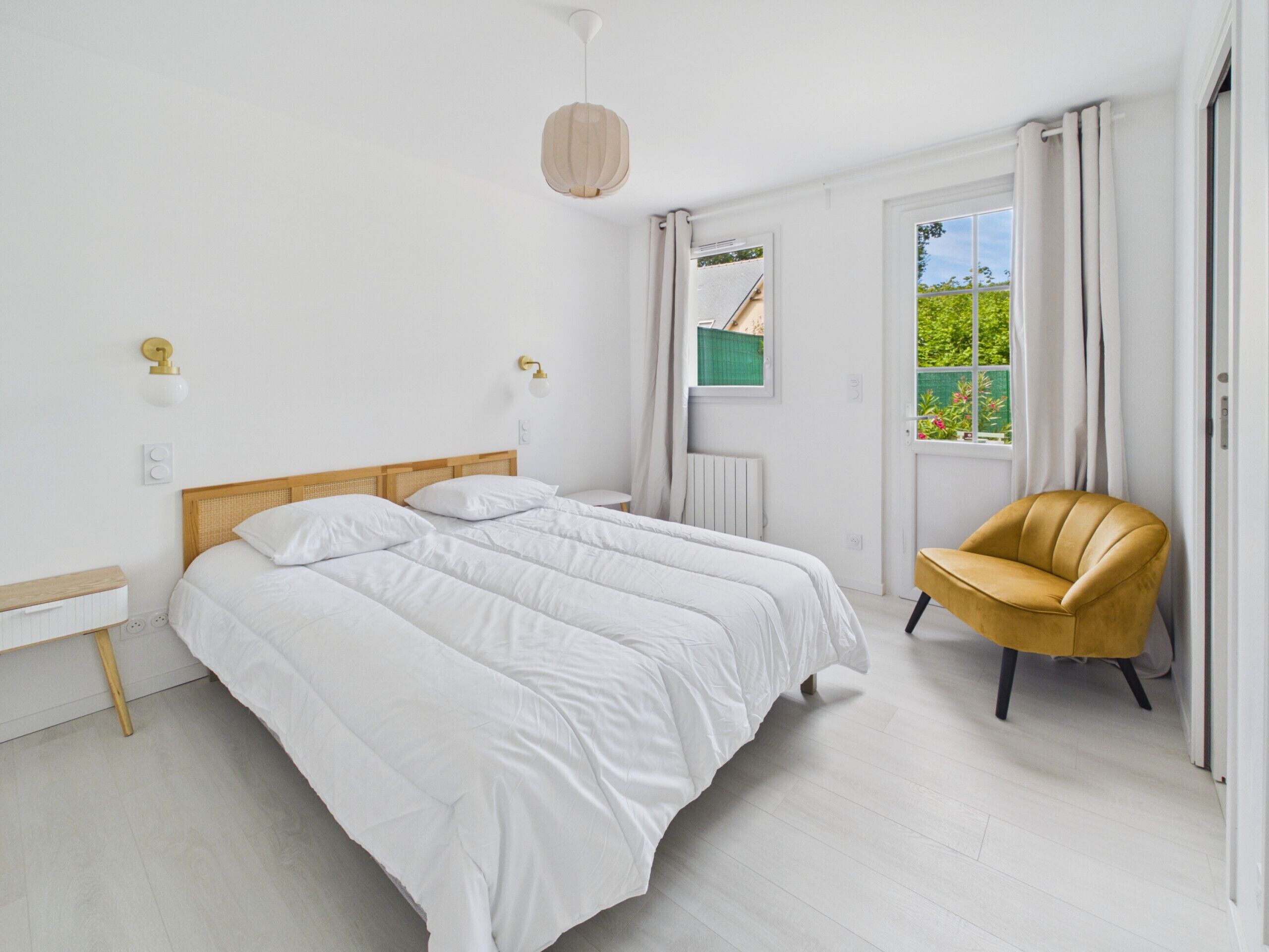 Ein Schlafzimmer mit einem Doppelbett, einem kleinen runden Tisch, einem Stuhl und einem Fenster mit Vorhängen.