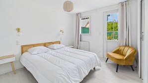 Un dormitorio con una cama doble, una mesita pequeña y redonda, una silla y una ventana con cortinas.