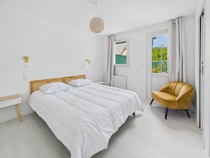 Ein Schlafzimmer mit einem Doppelbett, einem kleinen runden Tisch, einem Stuhl und einem Fenster mit Vorhängen.