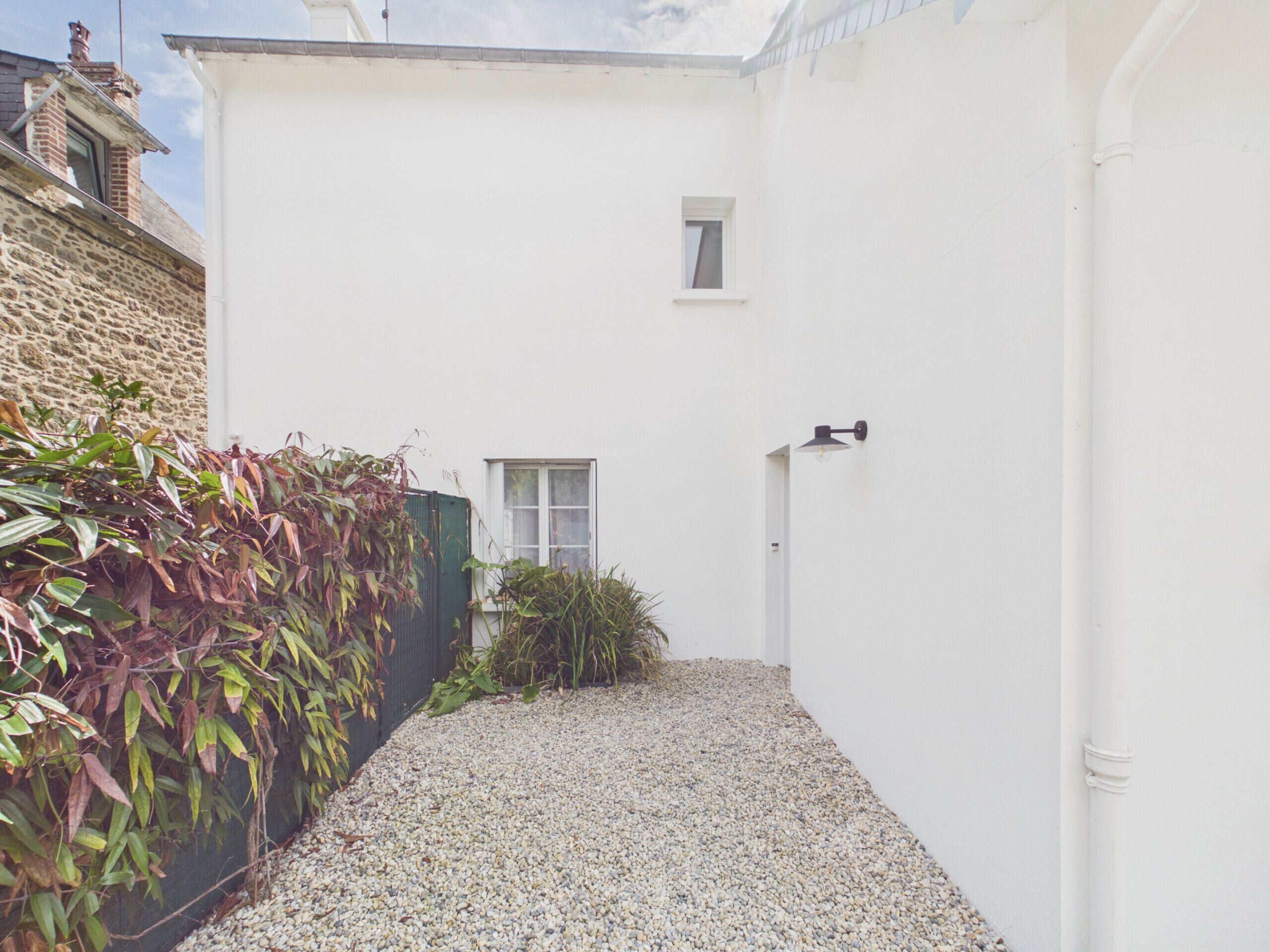 A narrow gravel path leading to a white building with a small window and a door.