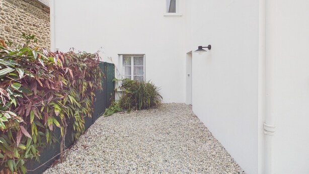 Un sendero de grava estrecho que conduce a un edificio blanco con una ventana pequeña y una puerta.