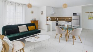 Una sala de estar moderna con un sofá verde, una mesa de centro blanca y una mesa de comedor de vidrio con sillas.