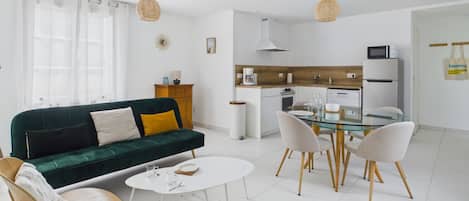 Ein modernes Wohnzimmer mit einem grünen Sofa, einem weißen Couchtisch und einem Esstisch aus Glas mit Stühlen.