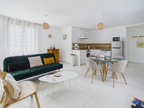Ein modernes Wohnzimmer mit einem grünen Sofa, einem weißen Couchtisch und einem Esstisch aus Glas mit Stühlen.
