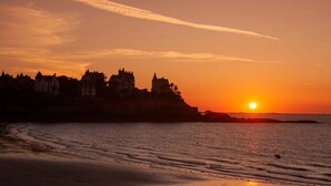 Un atardecer sobre una ciudad costera con edificios históricos silueteados contra el cielo.