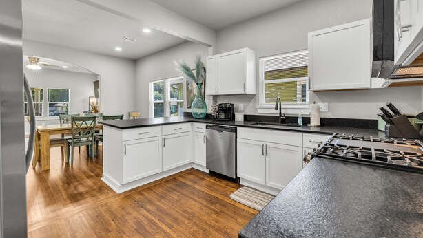 A modern kitchen with white cabinetry, a black countertop, and a stainless steel dishwasher. - 7th St Retreat-Tv's in Every Bedroom-Fully Fenced (Tulsa)