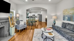 A modern living room with a fireplace, a dining area, and a kitchen in the background. - 7th St Retreat-Tv's in Every Bedroom-Fully Fenced (Tulsa)