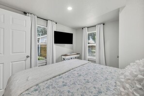 Un dormitorio con una cama, un televisor montado en la pared y una ventana con cortinas.