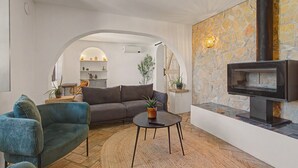 A living room with a sofa, armchair, and coffee table, a fireplace, and a kitchen visible through an archway.