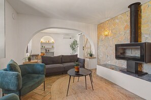 A living room with a sofa, armchair, and coffee table, a fireplace, and a kitchen visible through an archway.