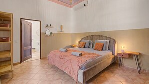 A bedroom with a bed, bedside tables, a wardrobe, and a door leading to another room.