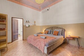 A bedroom with a bed, bedside tables, a wardrobe, and a door leading to another room.