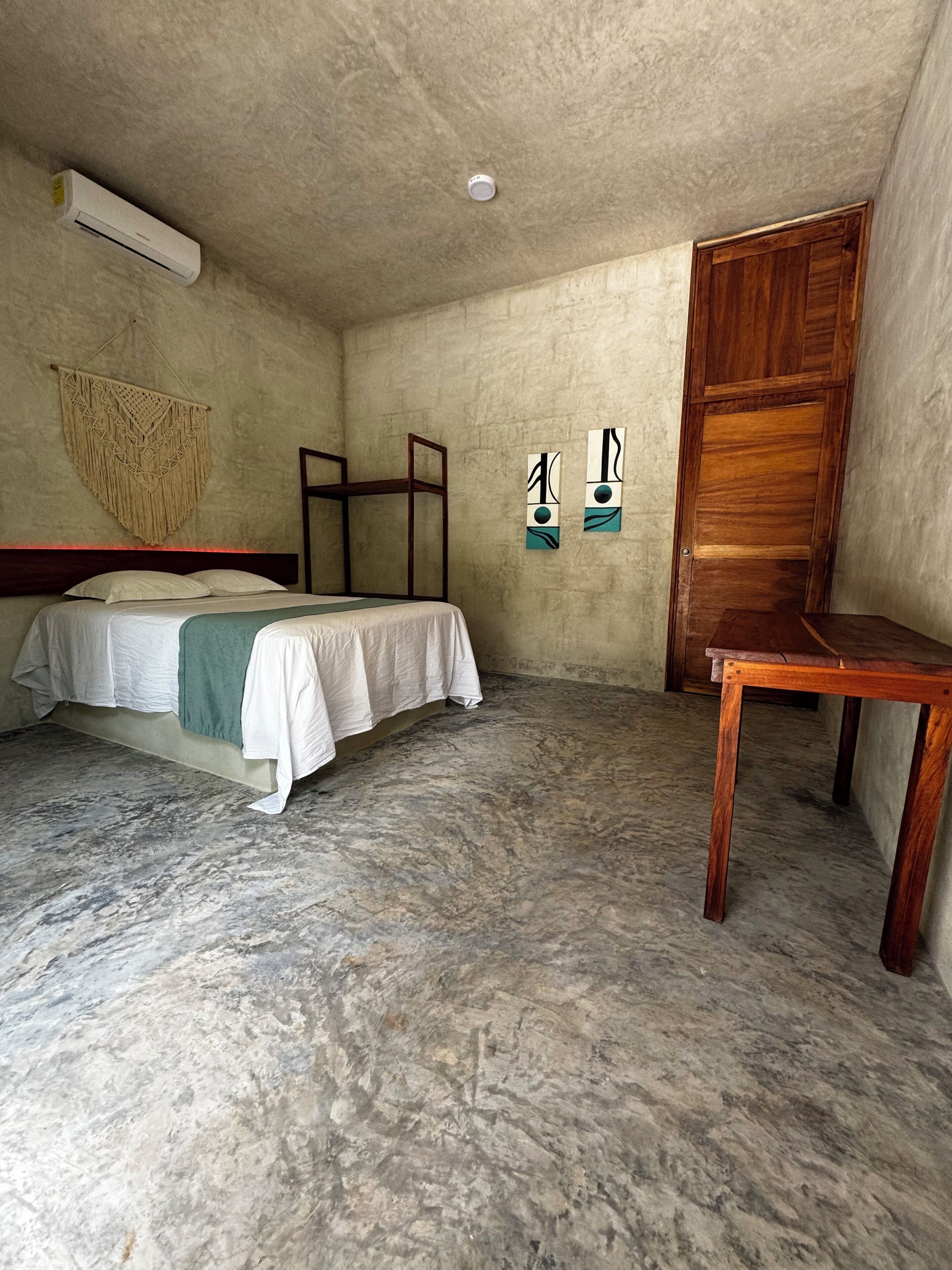 Um quarto com uma cama, uma mesa de madeira e um painel de macramê na parede.