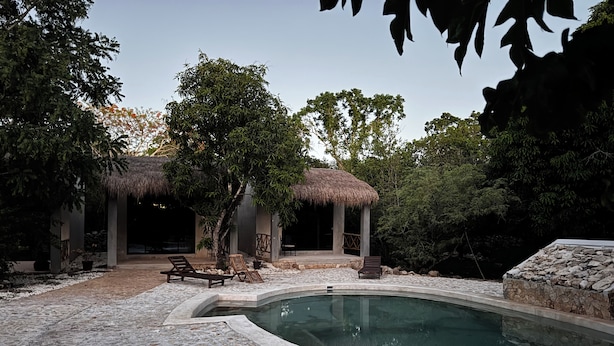 A pool area with a stone deck, lounge chairs, and a thatched-roof structure. - Hacienda Ticuch Valladolid (Valladolid)