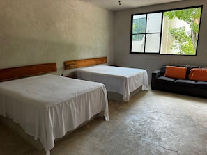 Een kamer met twee bedden, een slaapbank en een raam met uitzicht op groen.