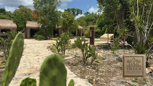 A courtyard with thatched-roof structures, cacti, and a sign for Hacienda Ticuch. - Hacienda Ticuch Valladolid (Valladolid)
