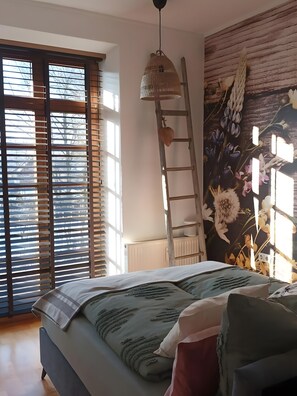 Un dormitorio con cama, escalera, lámpara de pared y ventana con persianas.