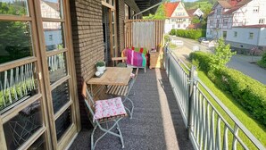 Een balkon met een tafel en stoelen, en uitzicht op de straat met huizen op de achtergrond.