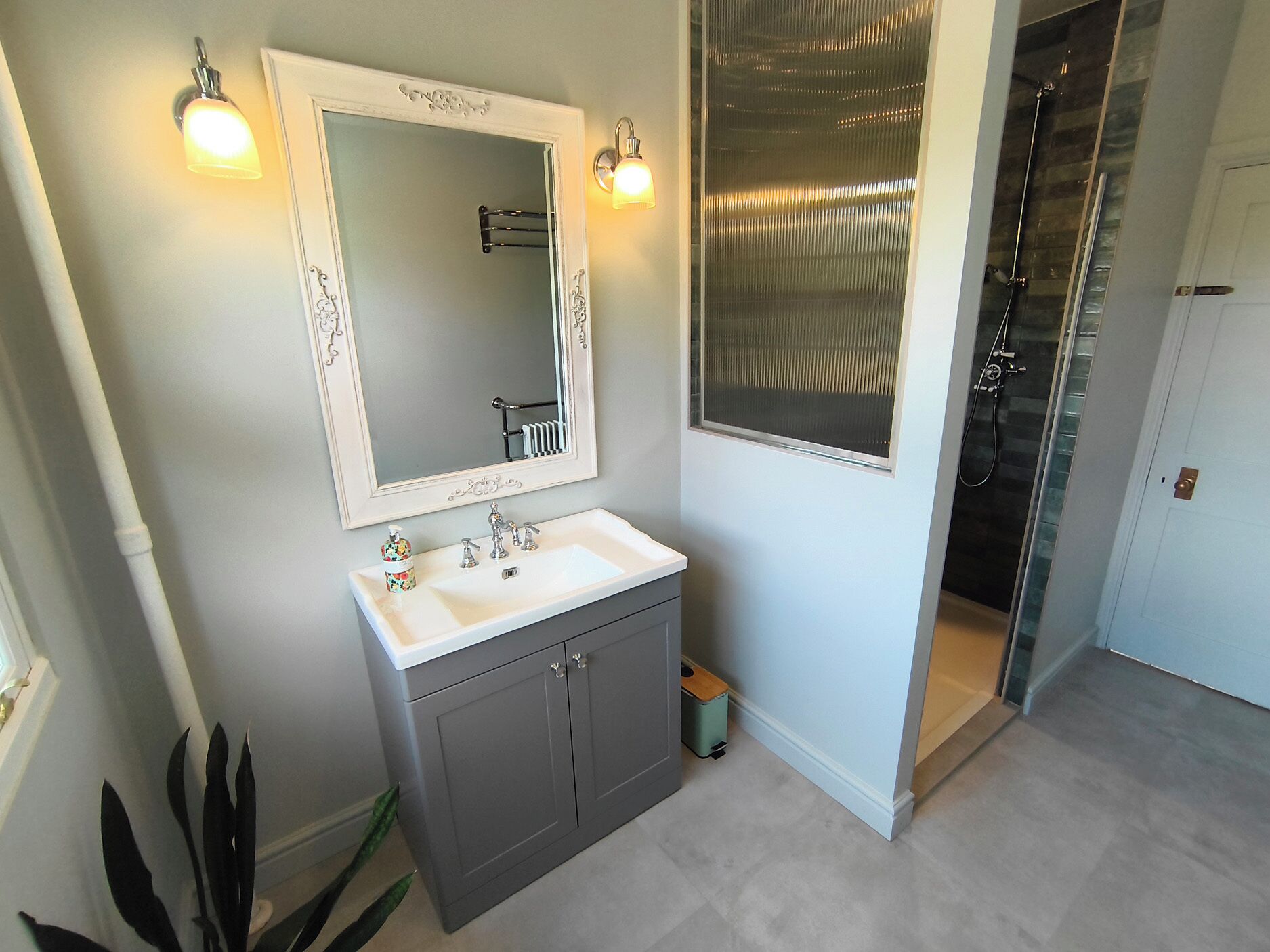 A bathroom with a white sink, a mirror with a decorative frame, and a shower area with a glass door.