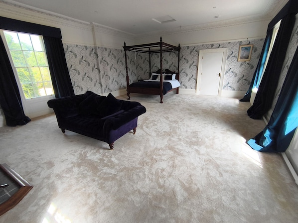 A spacious room with a large bed, a four-poster canopy, and a dark-colored sofa.