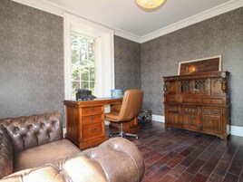 Una habitación con un sofá de cuero, un escritorio de madera, una máquina de escribir antigua y un armario de madera.