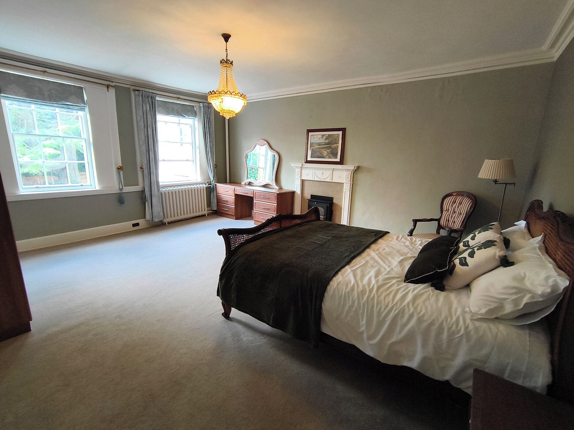 A bedroom with a large bed, a dresser, a mirror, a fireplace, and a chandelier.
