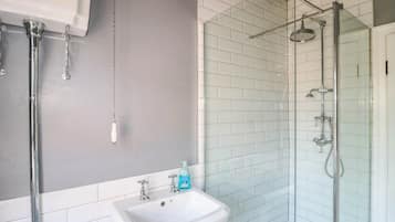 Un baño con lavamanos blanco, cabina de ducha de vidrio y pared de azulejos blancos.