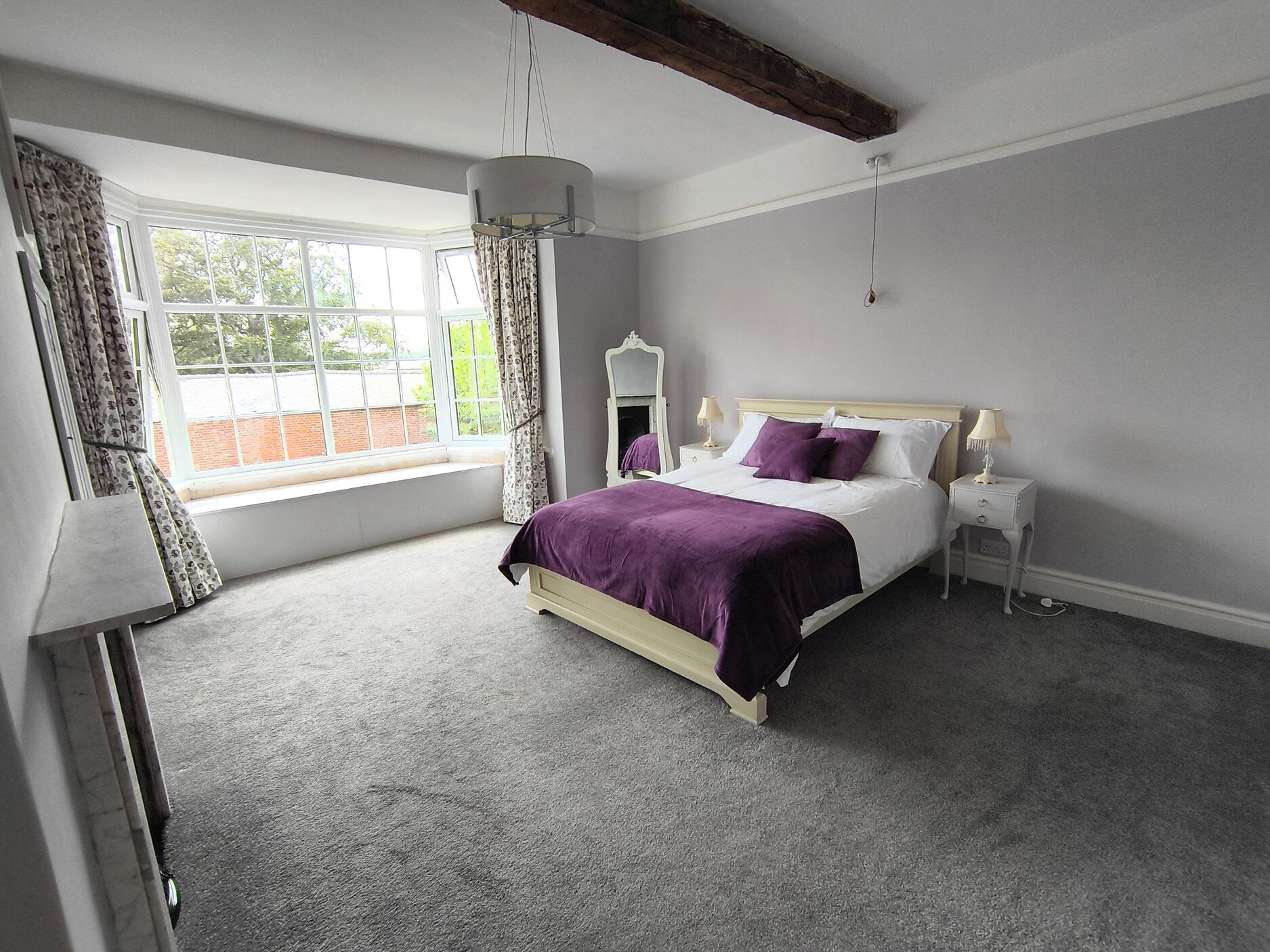 Een slaapkamer met een bed, nachtkastjes, een spiegel en een raam met gordijnen.