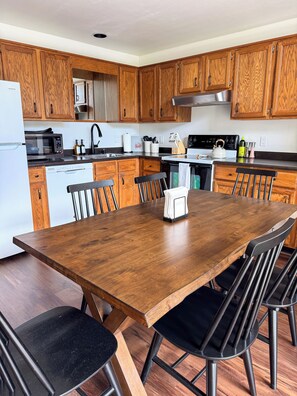 A modern kitchen with wooden cabinets, a stainless steel refrigerator, a microwave, a dishwasher, and a dining table with chairs. - Quiet Birch Bay Escape | Walk to Beach & Fun (Blaine)