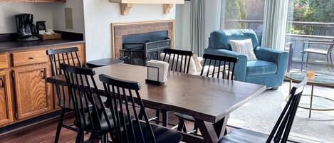 Una cucina moderna con armadietti in legno, un tavolo da pranzo con sedie, un camino e un'ampia finestra vista alberi.