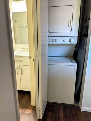 A compact laundry room with a washing machine and dryer, a small sink, and a door leading to another room.