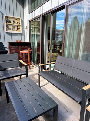 An outdoor seating area with two black metal tables and two grey cushioned benches. - Quiet Birch Bay Escape | Walk to Beach & Fun (Blaine)