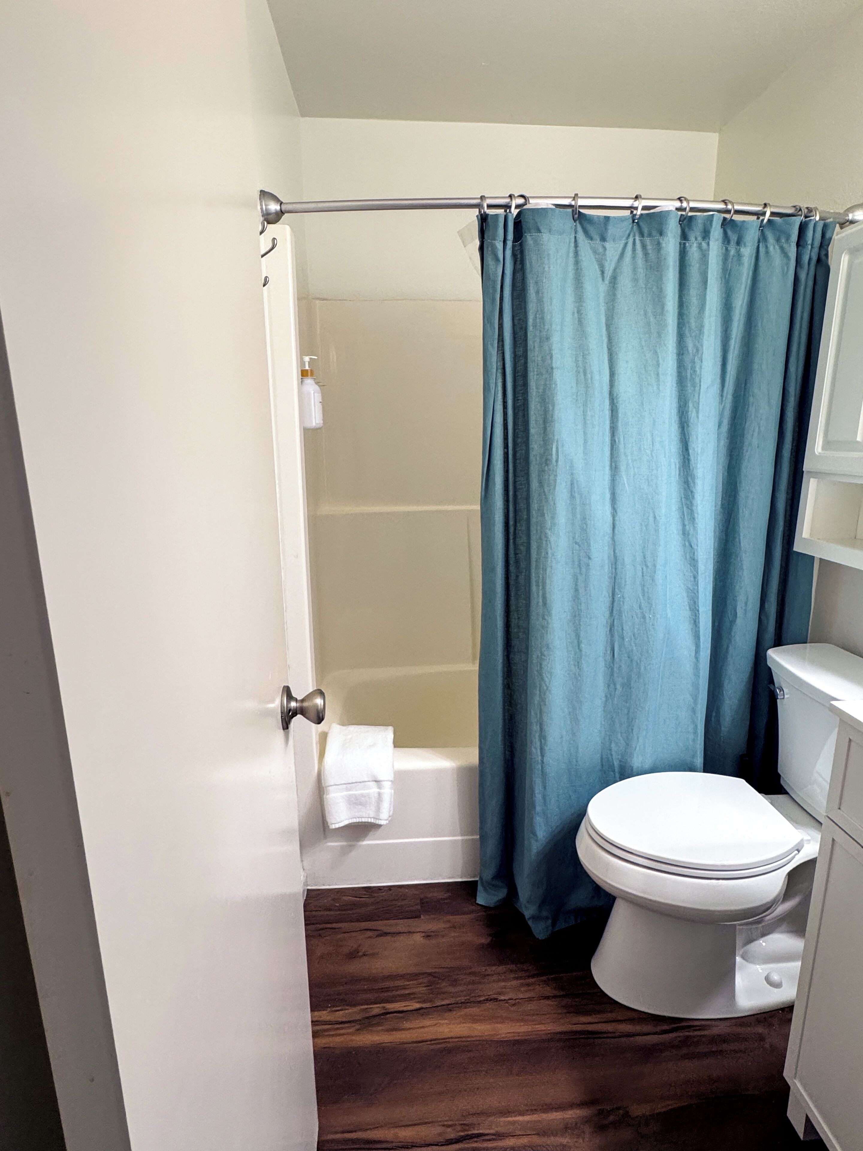 A bathroom with a white toilet, a bathtub, and a blue shower curtain.