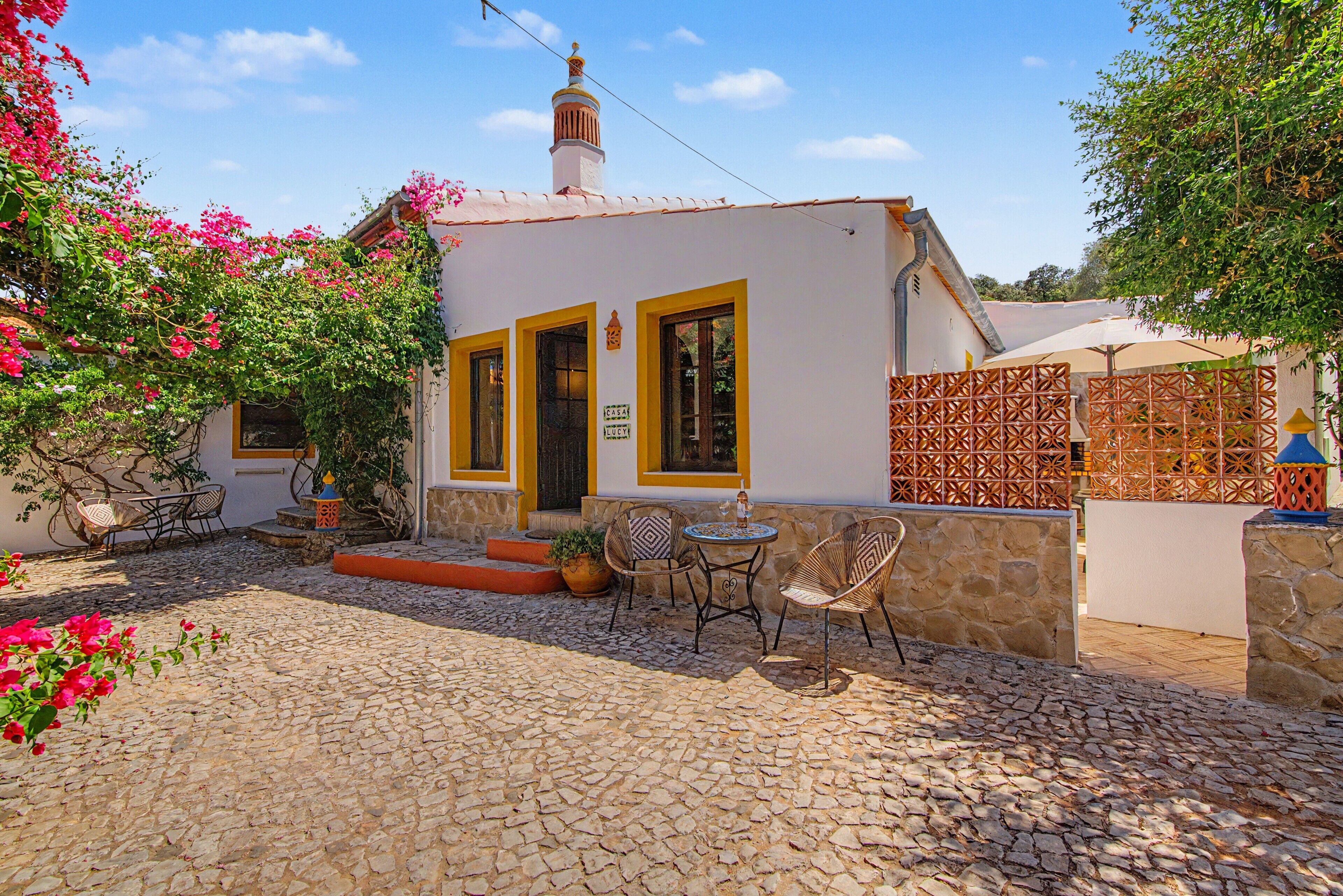 A small house with a cobblestone courtyard, a tiled patio, and a few outdoor chairs.