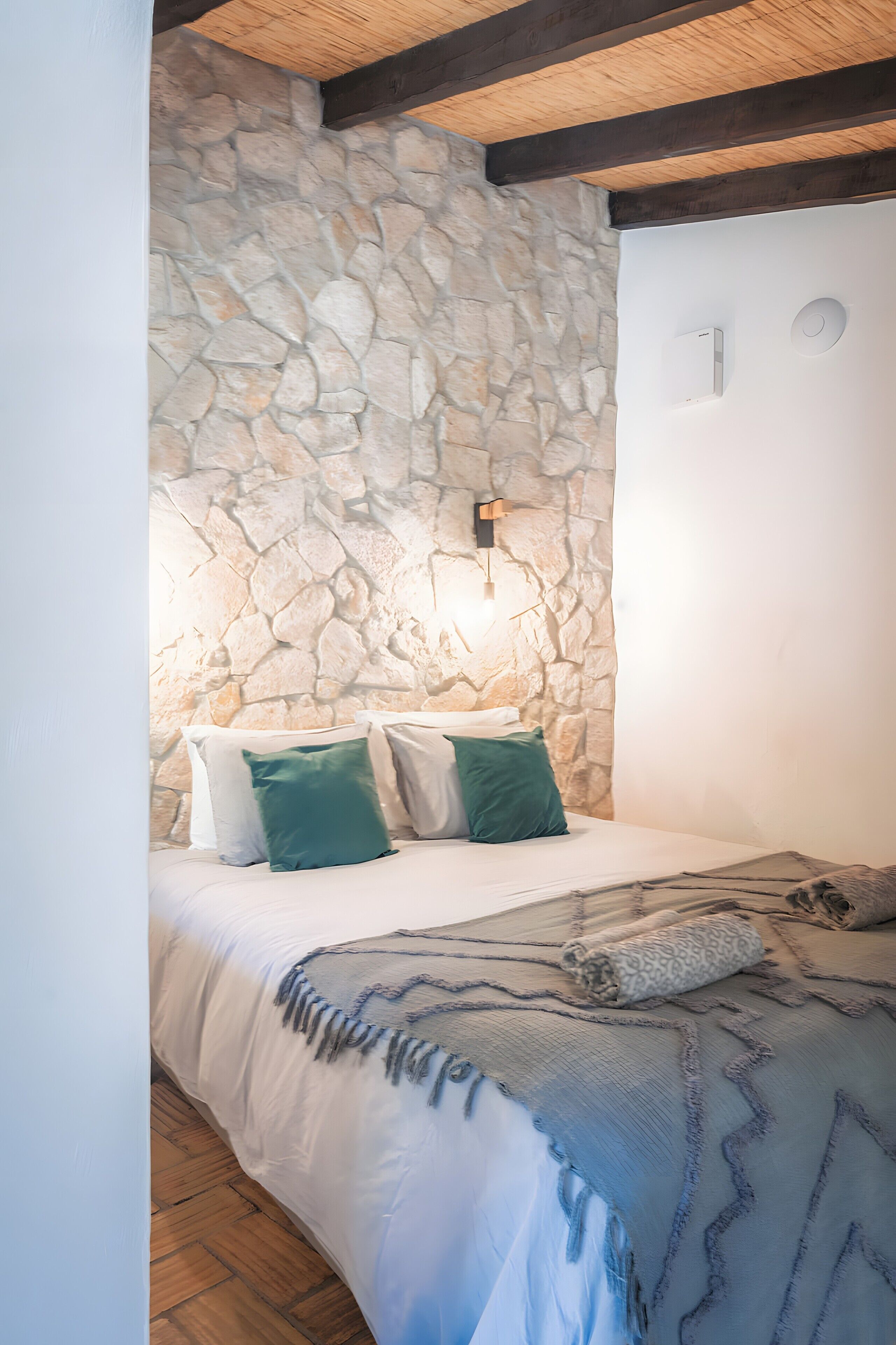 Ein Schlafzimmer mit Steinsturz, einem Bett mit weißer Bettwäsche und einer wandmontierten Leuchte.