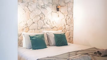 Ein Schlafzimmer mit Steinsturz, einem Bett mit weißer Bettwäsche und einer wandmontierten Leuchte.