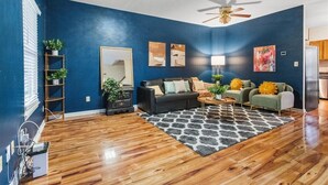 A living room with a blue wall, wooden flooring, a ceiling fan, a sofa set, a coffee table, and a rug. - 
Spacious 4BR Townhouse  Sleeps 13  Near DC&Metro (Arlington)