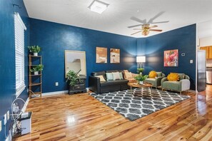 A living room with a blue wall, wooden flooring, a ceiling fan, a sofa set, a coffee table, and a rug. - 
Spacious 4BR Townhouse  Sleeps 13  Near DC&Metro (Arlington)