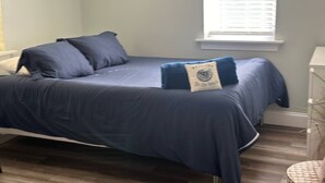 Quarto com cama, mesa de cabeceira, janela com persianas e uma obra de arte na parede.