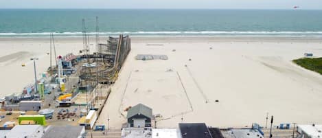 Vista frente al mar con una playa arenosa, un muelle con maquinaria de construcción y un edificio de techo plano en primer plano.
