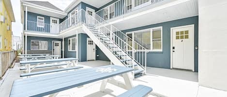A building with a staircase leading to a balcony, outdoor seating area with benches, and a door marked with the number 2.