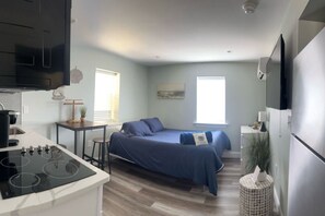 A compact room with a bed, a small table, a kitchenette with a stove, and a refrigerator. - Salty Shore Retreat: Idyllic Studio by the Sea (Wildwood)