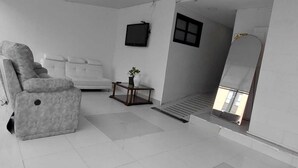 A modern living room with a grey sofa, a small table with a plant, and a television on the wall. - HOTEL SOFI CA BOUTIQUE (Bogotá)