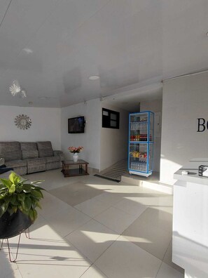Una sala de estar con un sofá, una mesita con un florero, un televisor y un mueble azul con agua embotellada.