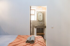Une chambre à coucher avec un lit, une salle de bain visible à travers une porte ouverte, et une serviette sur le lit.