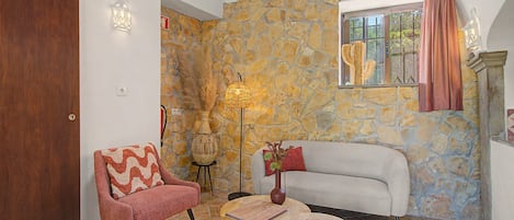 A living room with a stone wall, a sofa, a chair, a small table, and a lamp.