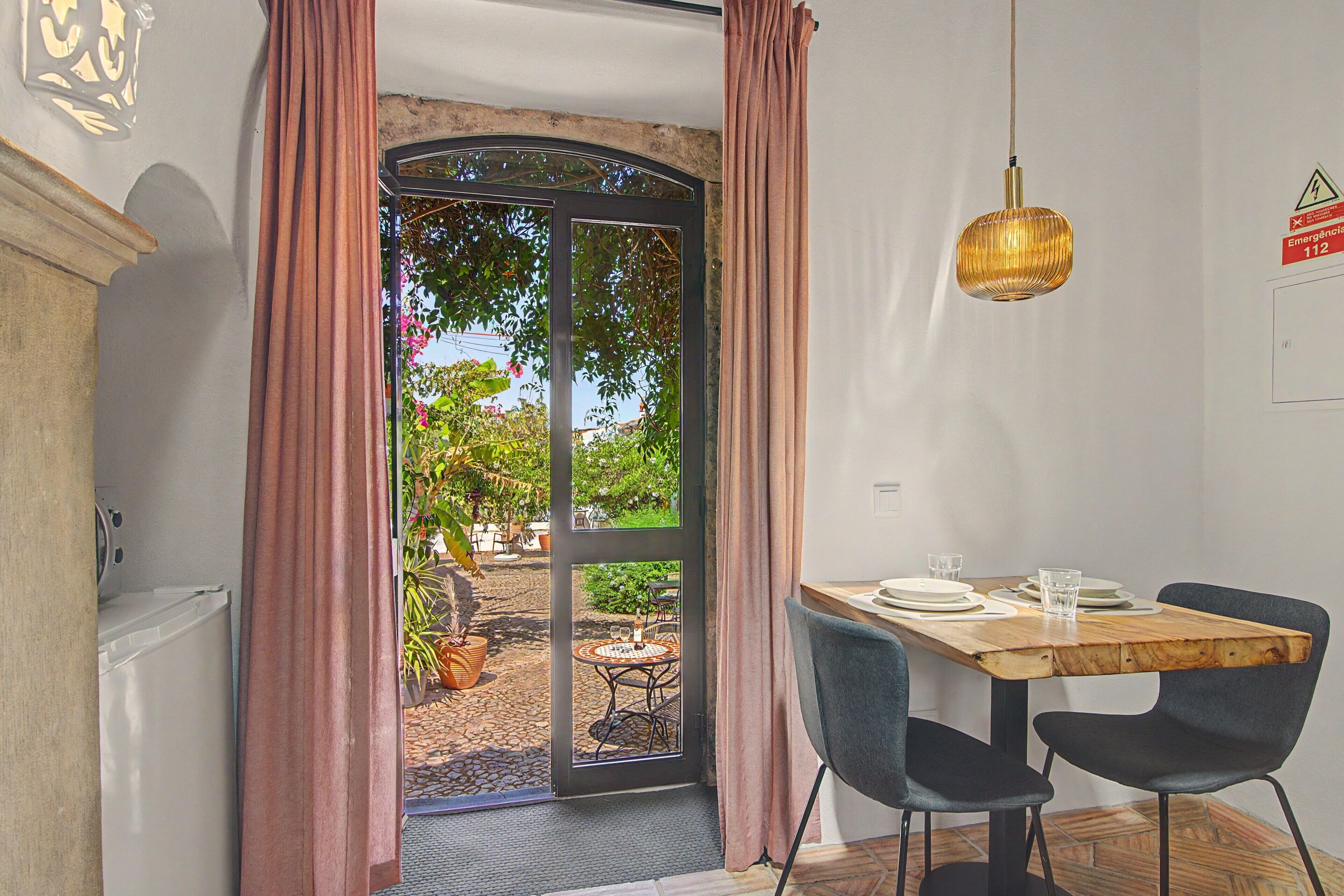 A room with a dining table, chairs, a hanging light fixture, and a view through a glass door.