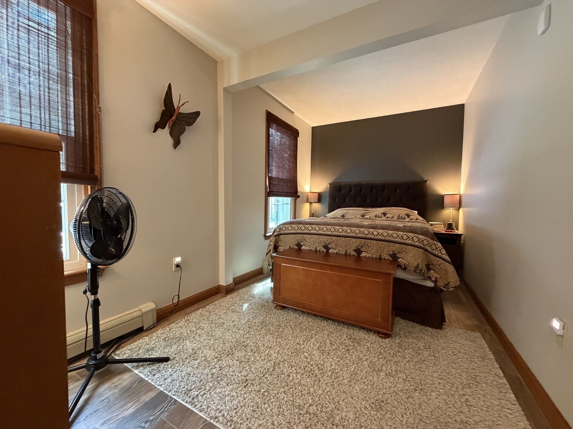 Quarto com cama, luminárias de cabeceira, ventilador e um objeto decorativo na parede.