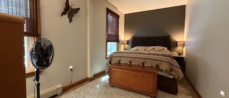 Une chambre à coucher comprenant un lit, des lampes de chevet, un ventilateur sur pied et un élément décoratif mural.