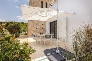 Eine Terrasse im Freien mit Tisch und Stühlen, einem weißen Sonnenschirm und einem Gebäude mit Steinwänden.